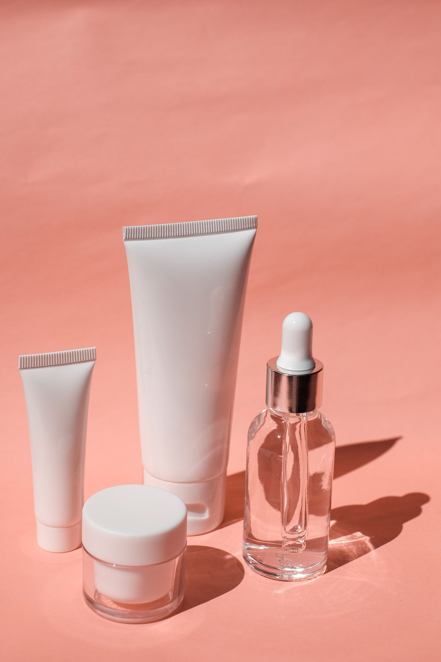 Serum Bottle, Cosmetic Tubes and Container on Pink Background